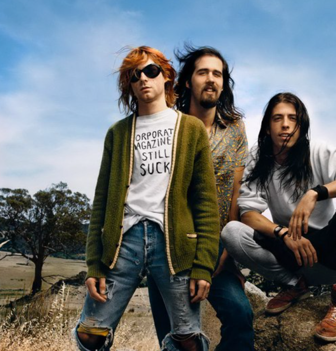 The image of three men, Kurt Cobain, Krist Novoselic, and Dave Grohl, all members of the iconic alternative rock and punk rock grunge band Nirvana, with Kurt Cobain famously wearing a white t-shirt with the slogan "Corporate Magazines Still Suck". References the cover of Rolling Stone on April 16th, 1992, when Nirvana was a new rock band, after their album "Nevermind" blew up in popularity.