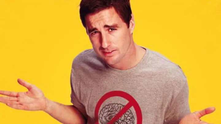 A man wearing a gray t-shirt with a red "no" symbol on it, making a hand gesture, against a yellow background.