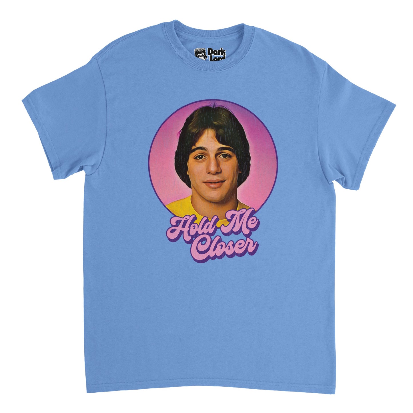 A vintage, souvenir blue colored short sleeved t-shirt that says "Hold Me Closer" in purple and pink bubble letters beneath an image a young Tony Danza, a professional boxer and actor famous for his role on the TV show "Who's the Boss?". In reference to the song 'Tiny Dancer' by Elton John which has lyrics that are often misheard as "Hold me closer, Tony Danza" or "Hold me close young Tony Danza", which is famously mentioned by the character Pheobe in an episode of the TV show "Friends".
