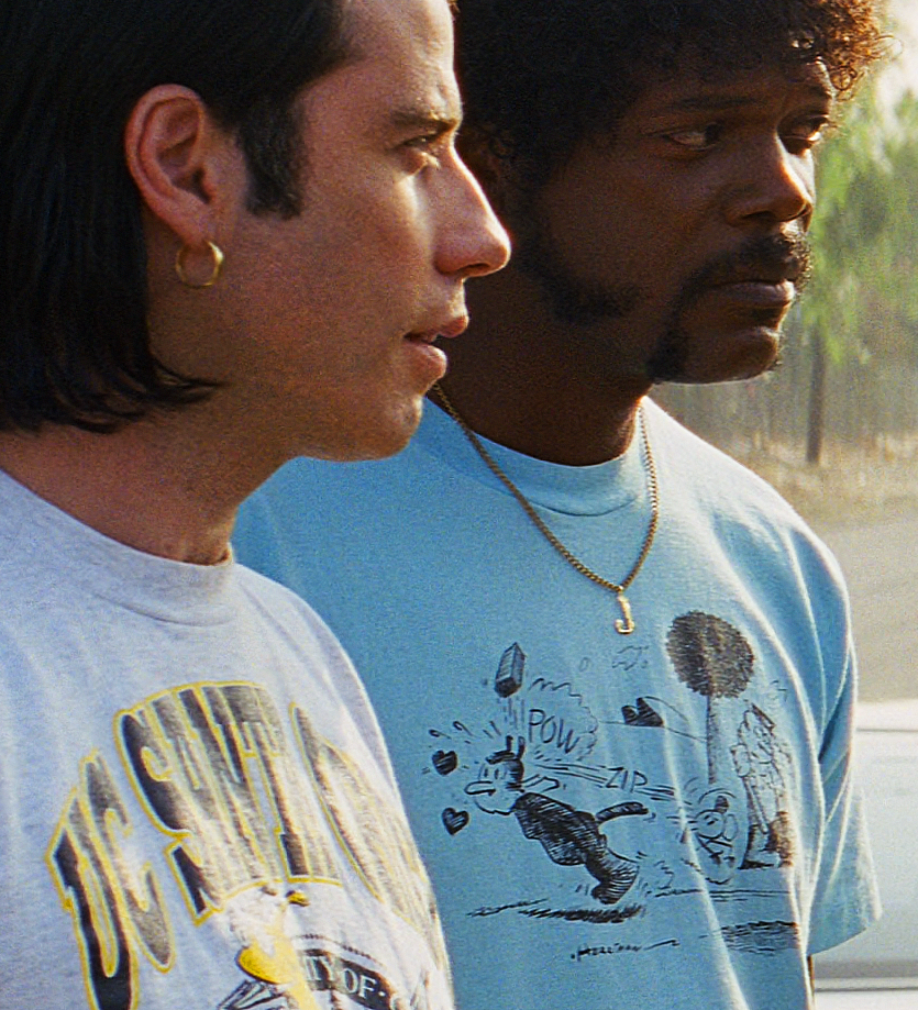 Two men standing side by side, one wearing a white t-shirt with a graphic and the other wearing a blue t-shirt with a cartoon character.