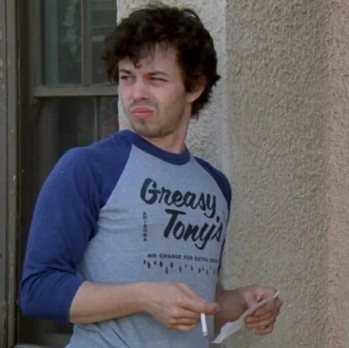 A man wearing a blue and gray shirt with the text "Greasy Tony's" is shown in the image.