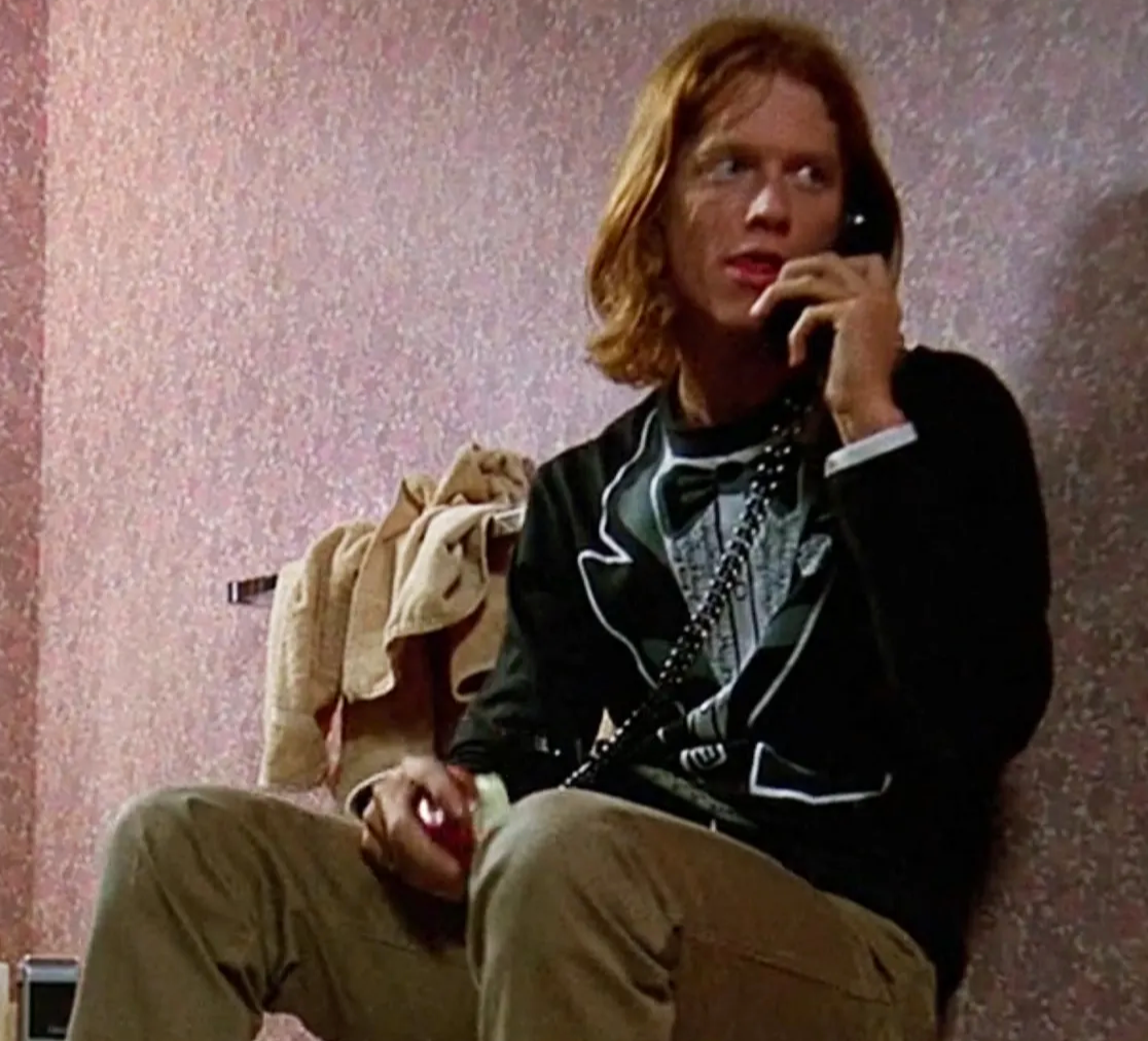 A man with long hair is sitting on a bench and talking on a phone.