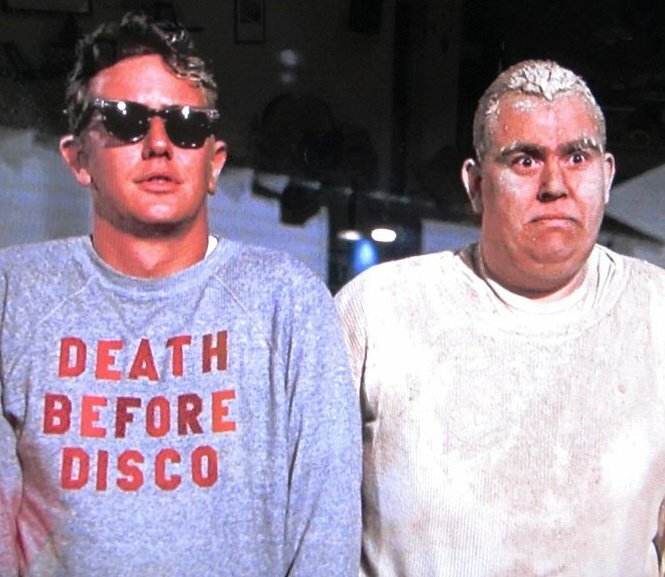 two men standing next to each other, one wearing a gray sweatshirt with the text "DEATH BEFORE DISCO" and the other wearing a white sweatshirt.