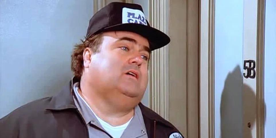 a man wearing a black baseball cap with the word "FLASK" on it, standing in front of a door.