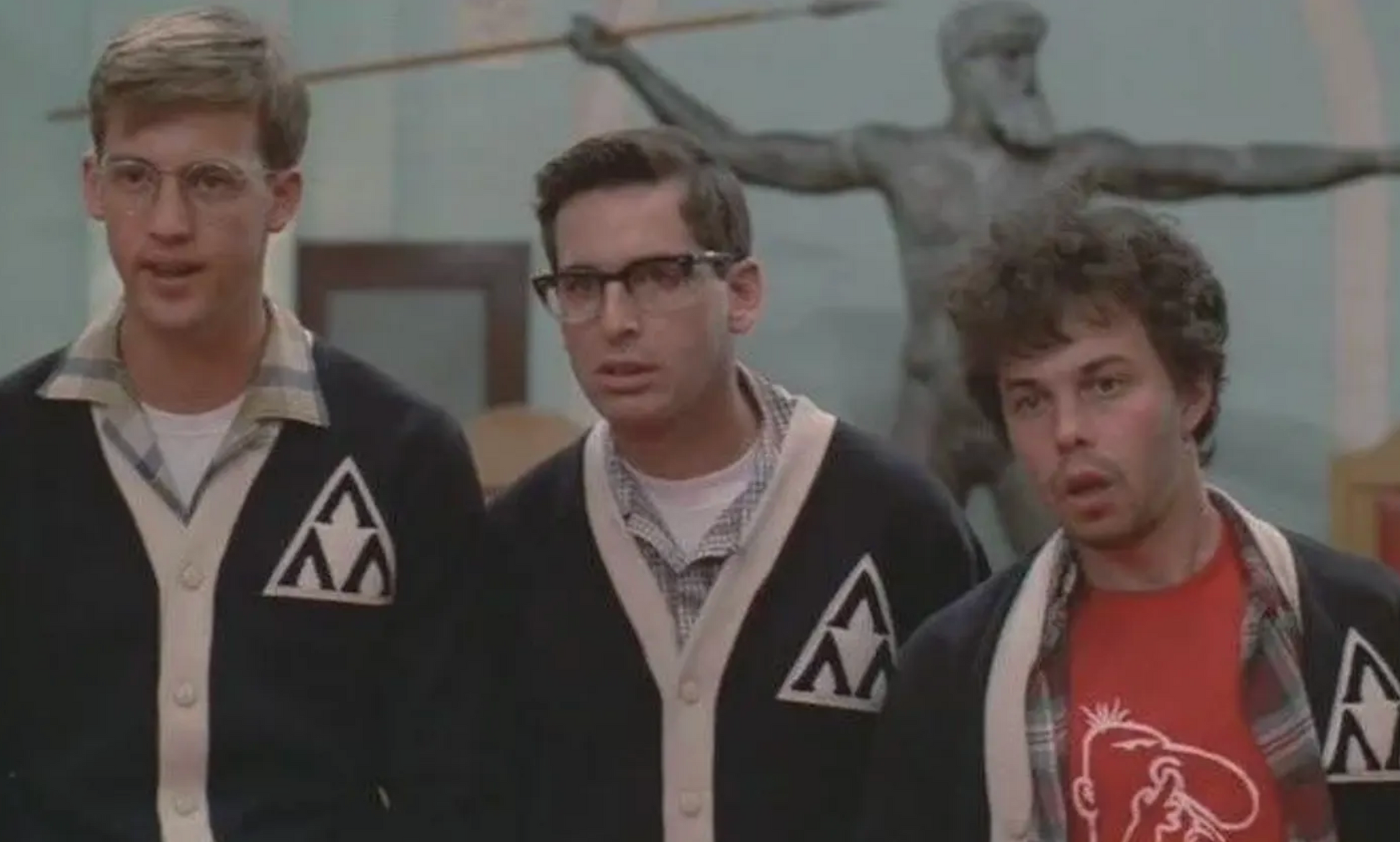 three young men standing together, with one of them wearing glasses and a black jacket with a white triangle on the left side.
