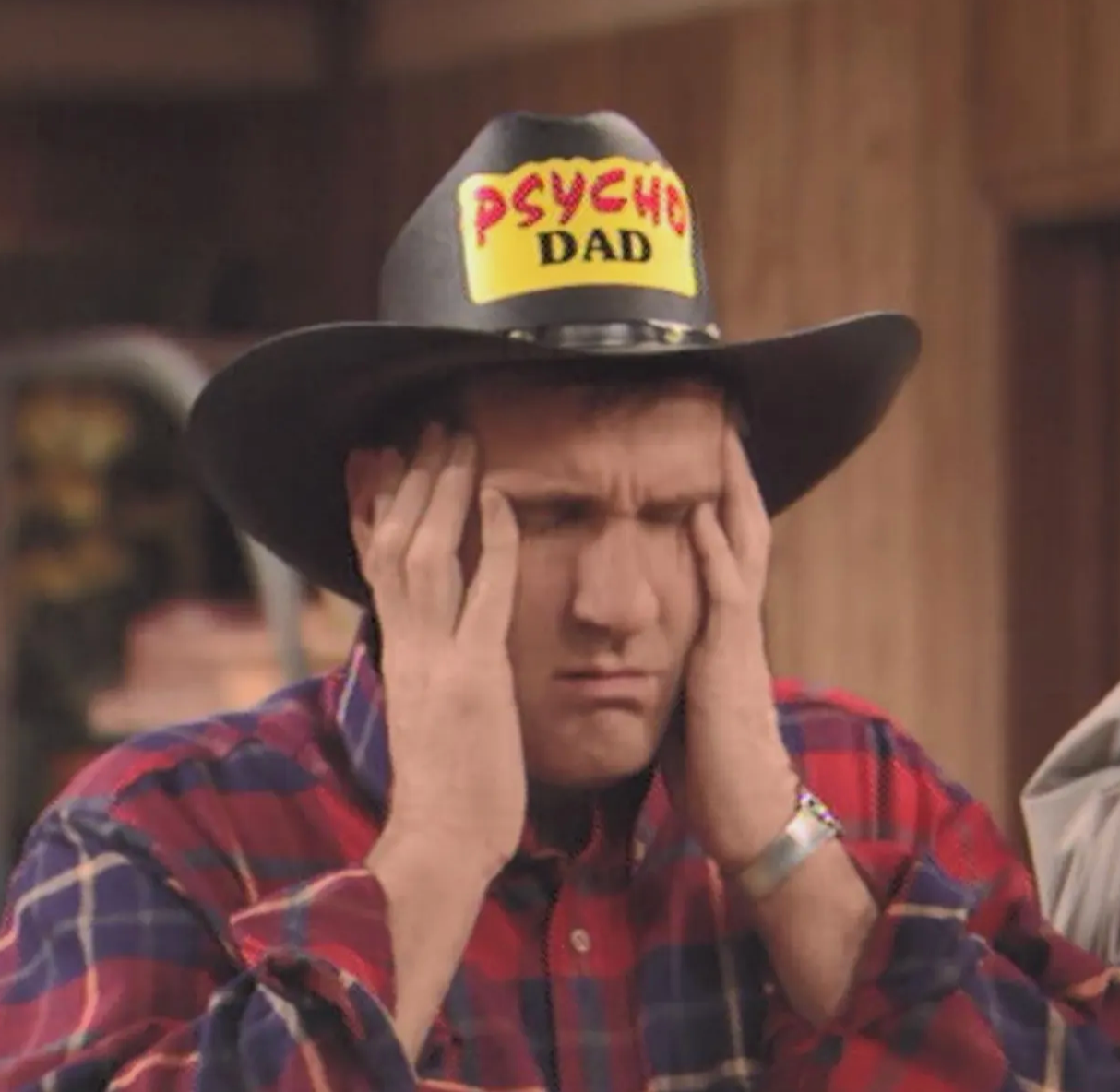A man wearing a cowboy hat with the words "PSYCHO DAD" printed on it, with his hands on his face, appears to be in a contemplative or distressed state.
