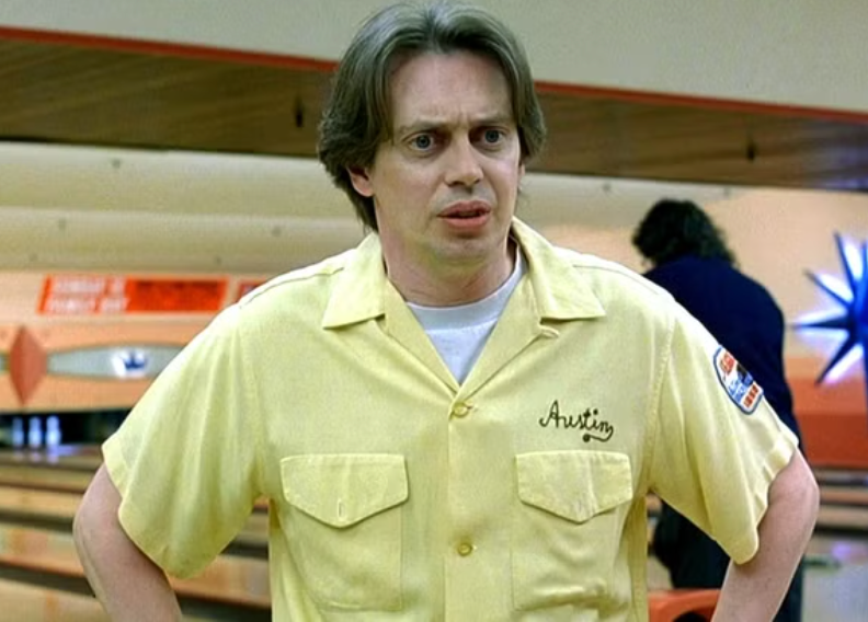 A man wearing a yellow shirt with the word "Aristotel" on it, standing in a bowling alley.