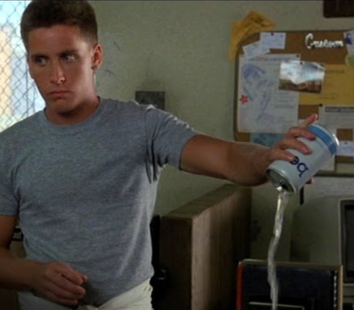 A man in a gray t-shirt is shown pouring liquid from a can into a glass, with a serious expression on his face.