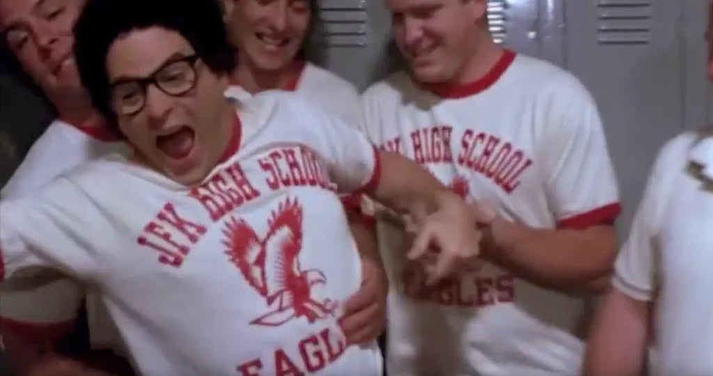 A group of people wearing white and red high school uniforms, with one person making a silly face and another person reaching out to him.
