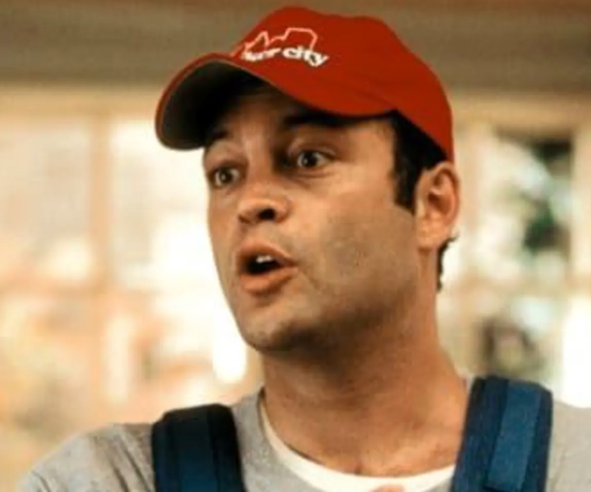A man wearing a red baseball cap with the word "HARDCORE" on it, looking off to the side with a serious expression.