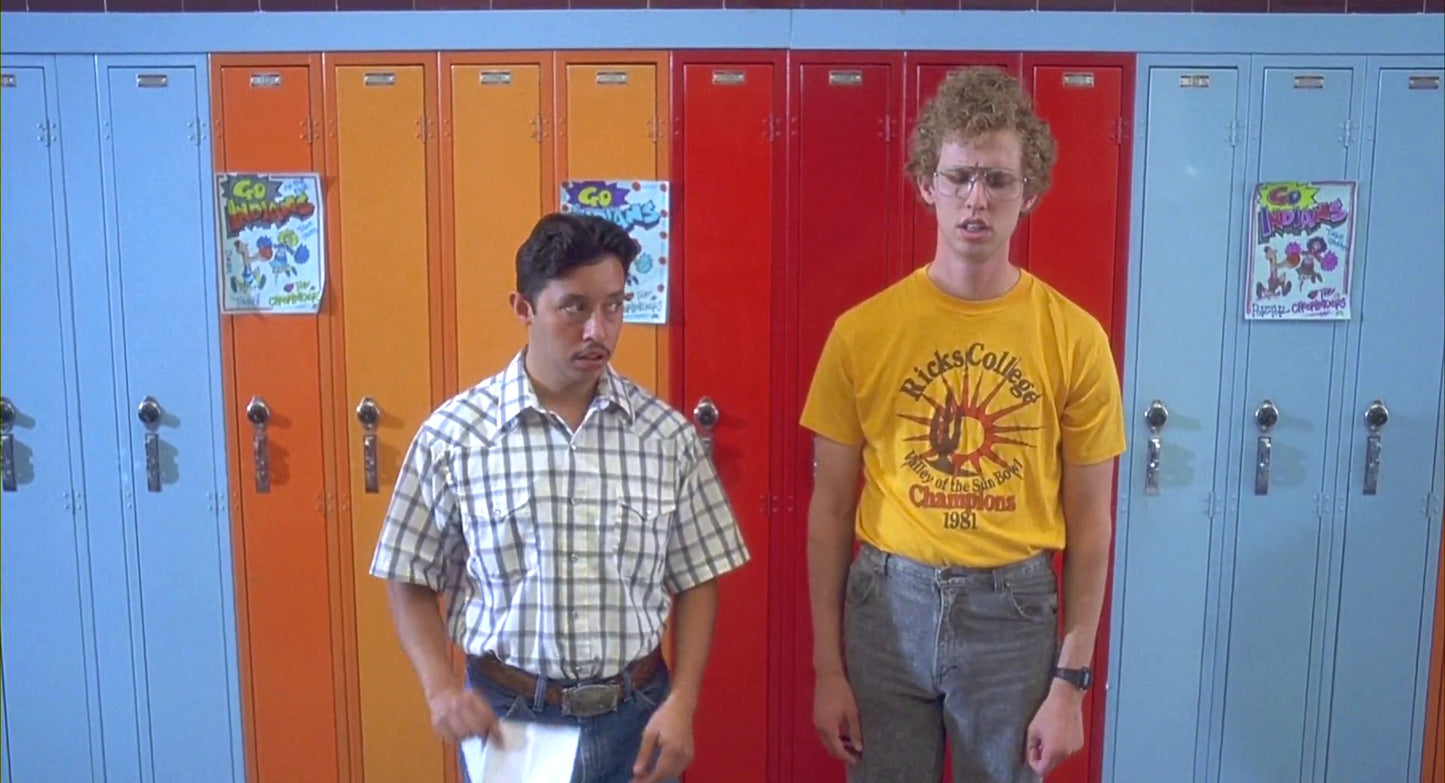 two men are standing in front of a row of colorful lockers. The man on the left is wearing a plaid shirt, while the man on the right is wearing a yellow t-shirt with a graphic design.