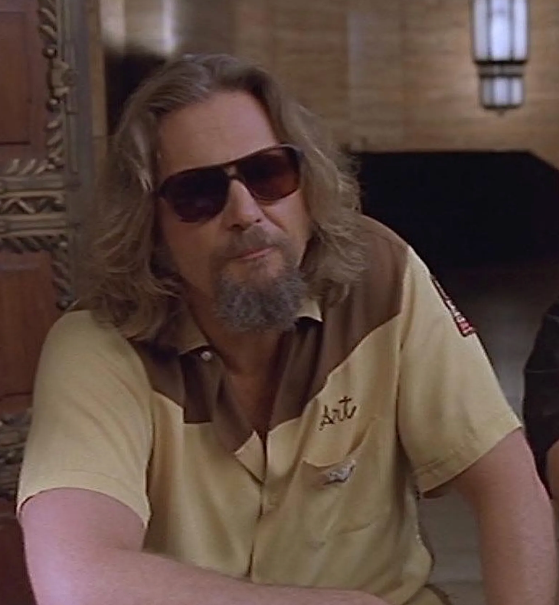 A man with long hair and sunglasses is sitting in a room, looking directly at the camera.