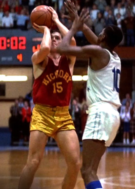 A basketball player in a red jersey with the number 15 is attempting a shot while being defended by a player in a white jersey with the number 10.