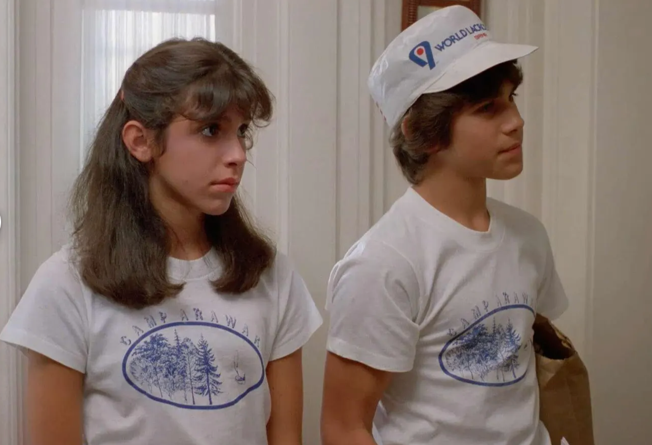 two people wearing matching white t-shirts with a blue design, standing together in a room.