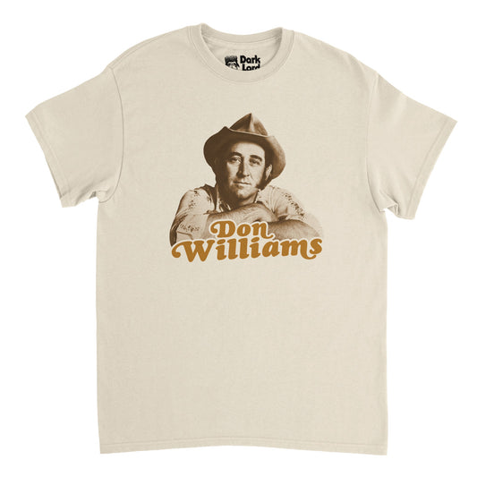 A retro, soft cream 1970s style t-shirt that says "Don Williams" in orange text with an image of the iconic American country music singer and songwriter and actor known as the "Gentle Giant" in the country music scene with hits like "I believe in You", "Tulsa Time", "Love Me Over Again", and "Love Is On A Roll". Also famous for being inducted into the Country Music Hall of Fame and 