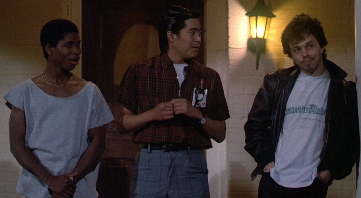 three men standing together in a doorway, with one man in the middle wearing a plaid shirt and the other two men on either side wearing casual clothing.