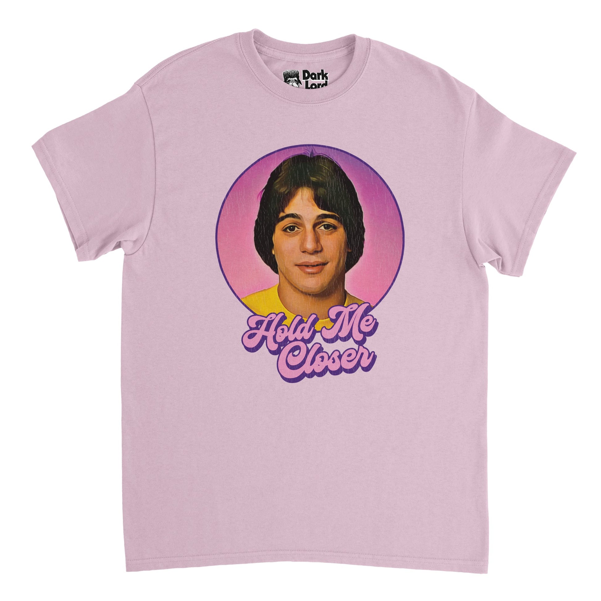 A retro, 80s style light pink t-shirt that says "Hold Me Closer" in purple and pink bubble letters beneath an image of actor and retired professional boxer Tony Danza, famous for his role on sitcom "Who's the Boss?". References the Elton John song "Tiny Dancer" with lyrics often misheard as "Hold me closer, Tony Danza" or "Hold me close young Tony Danza", famously quoted by character Pheobe in an episode of the American television sitcom "Friends". 
