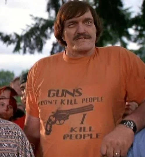 A man wearing an orange t-shirt with the text "GUNS DON'T KILL PEOPLE I KILL PEOPLE" printed on it.