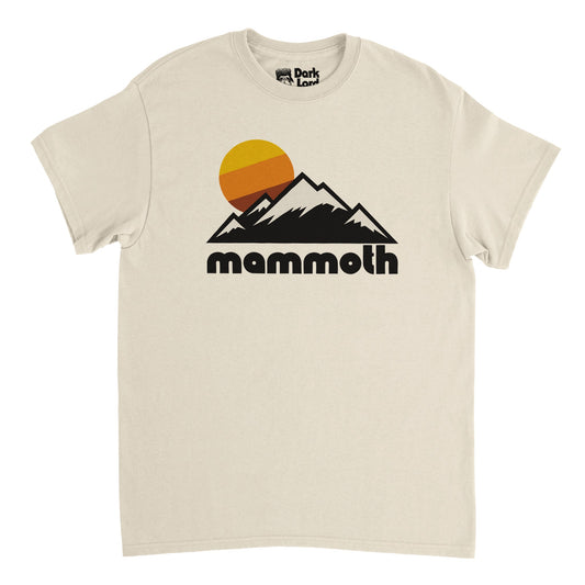 A soft cream colored vintage, 80s style t-shirt that says "mammoth" in bold, black bubble letters underneath the image of multiple snow covered mountain peaks, an aesthetic yellow/orange/reddish brown sun setting. In reference to California's Mammoth Mountain, home to Mammoth Mountain Ski Area and ski and snowboard resort, located in the stunning Sierra Nevada Range with incredible mountain views, hiking and backpacking opportunities, and winter sports. 